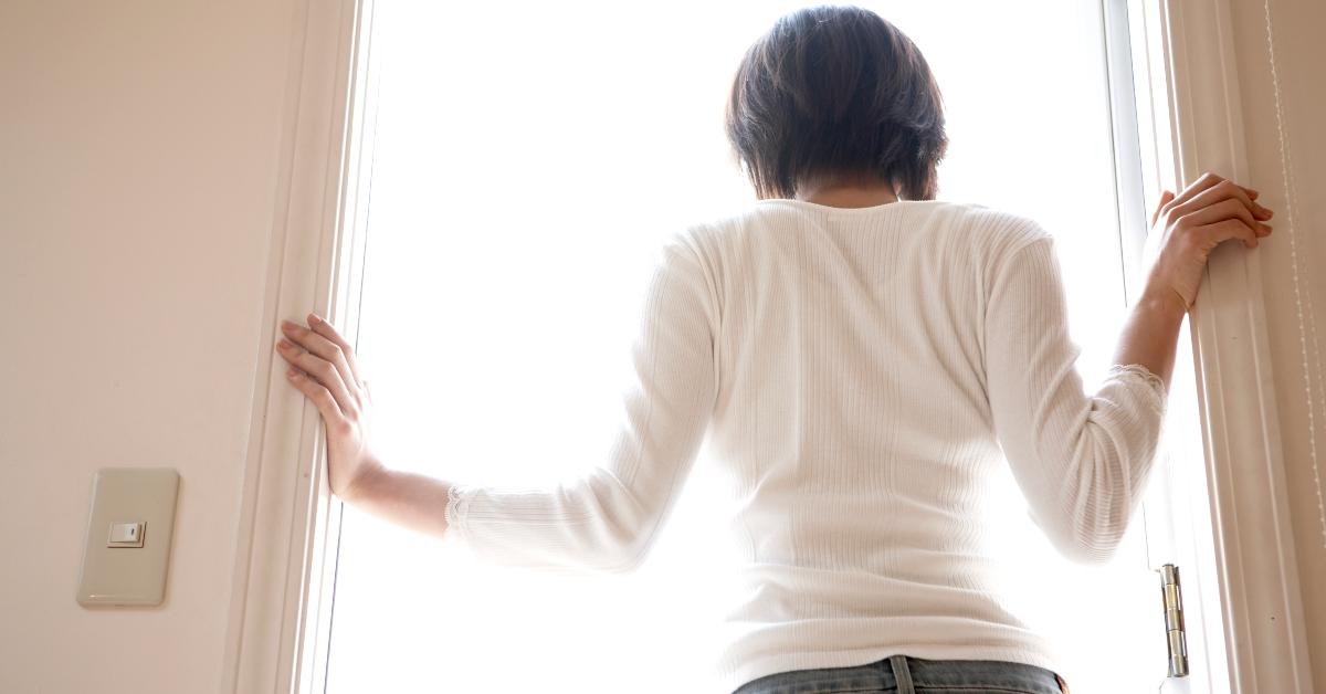 woman in white shirt looks out of door