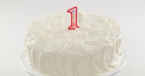 Stock image of a first birthday cake covered in vanilla frosting with a red #1 candle on top