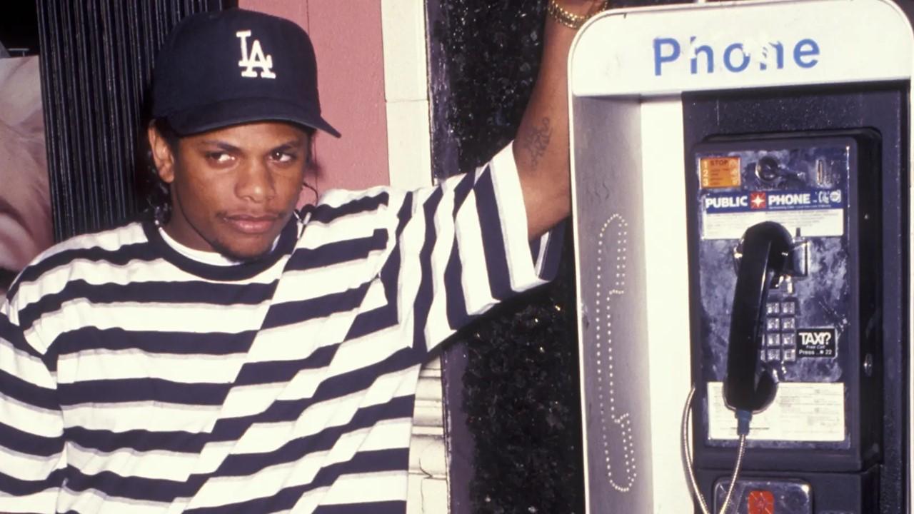 Rapper Eazy-E poses next to phone booth. 