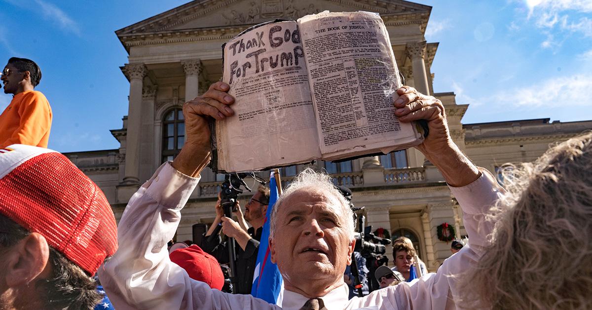 A man holding a Bible that says 'Thank God for Trump' during a protest. 