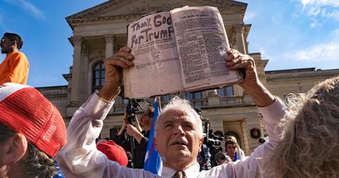 A man holding a Bible that says 'Thank God for Trump' during a protest.