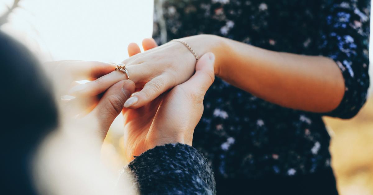 A man slides an engagement ring on his lady's finger.