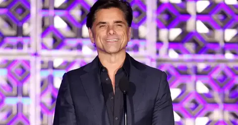 John Stamous in a black suit on-stage with a microphone