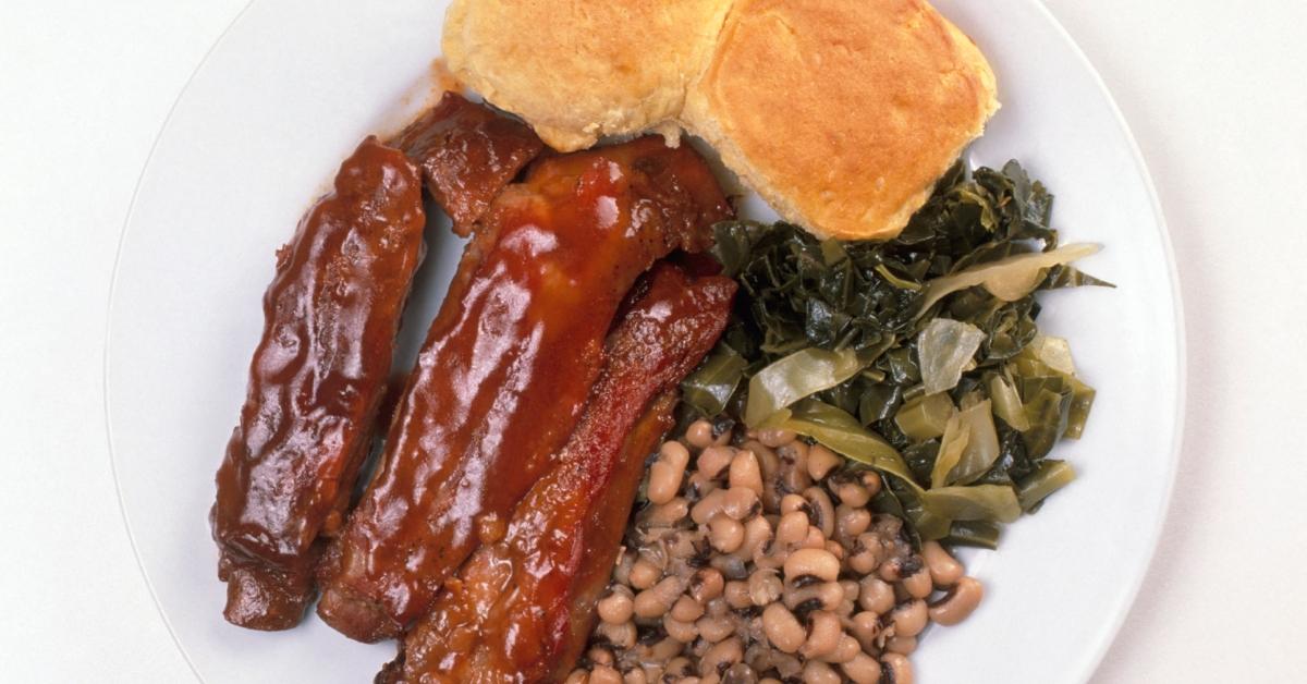 A stock photo of a plate of ribs, cornbread, collard greens, and black eyed peas