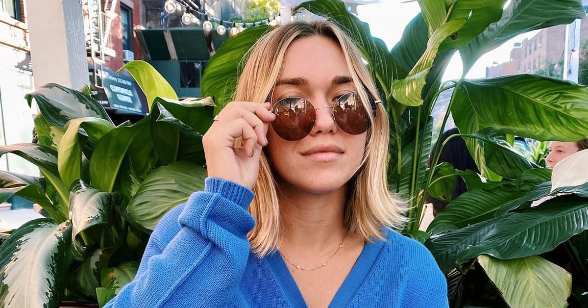 Photo of TikTok creator Megan Boni wearing round sunglasses and a blue cardigan and sitting in front of a plant