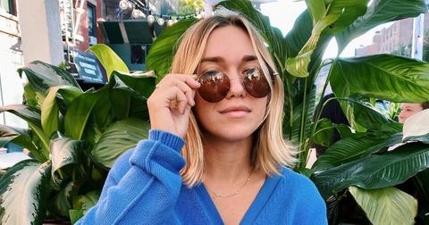 Photo of TikTok creator Megan Boni wearing round sunglasses and a blue cardigan and sitting in front of a plant