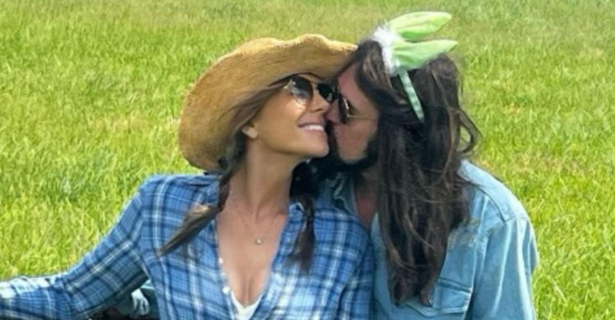 Elizabeth and Billy Ray lean against a wood fence as he plants a kiss on her cheek.