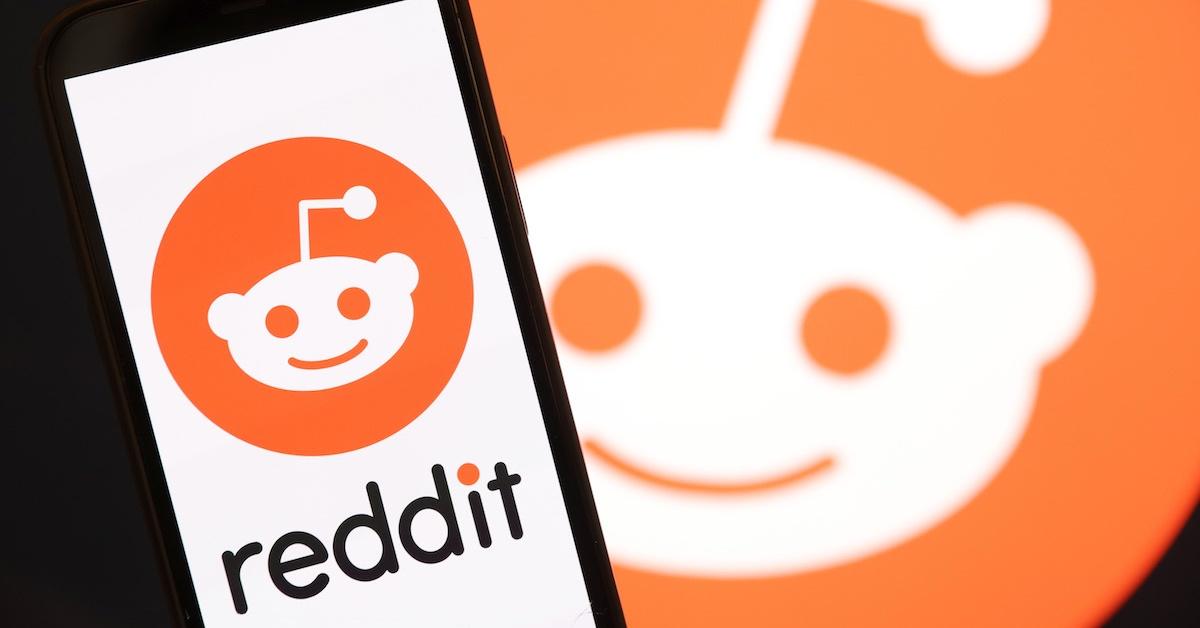A Reddit logo on a phone and the company logo in the background