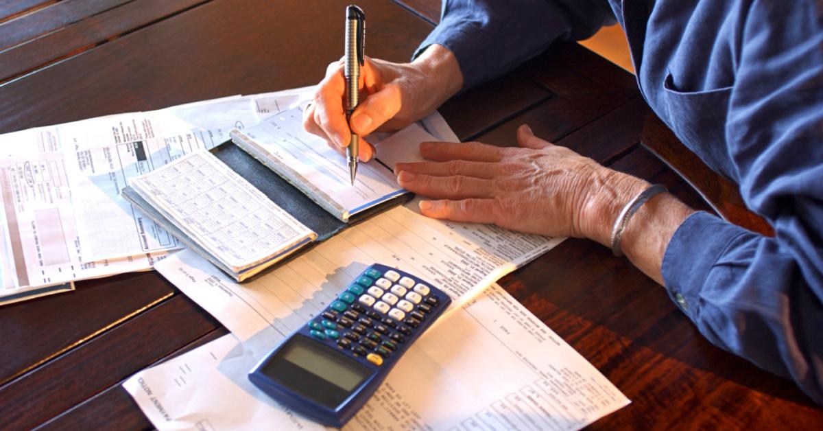 Close-up of a mature woman's hands as she sits at a table writes checks