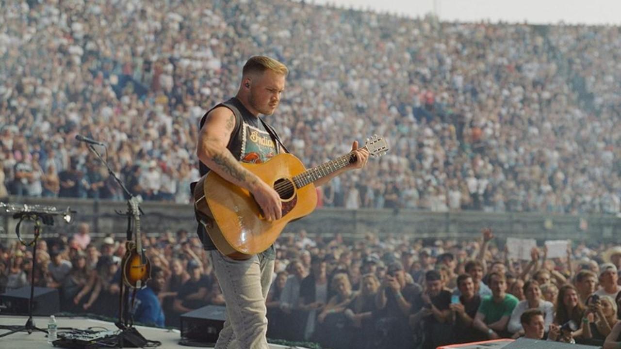 Zach Bryan playing his guitar onstage during a concert