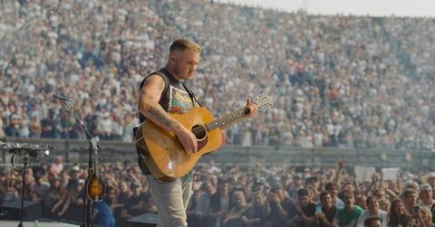 Zach Bryan playing his guitar onstage during a concert