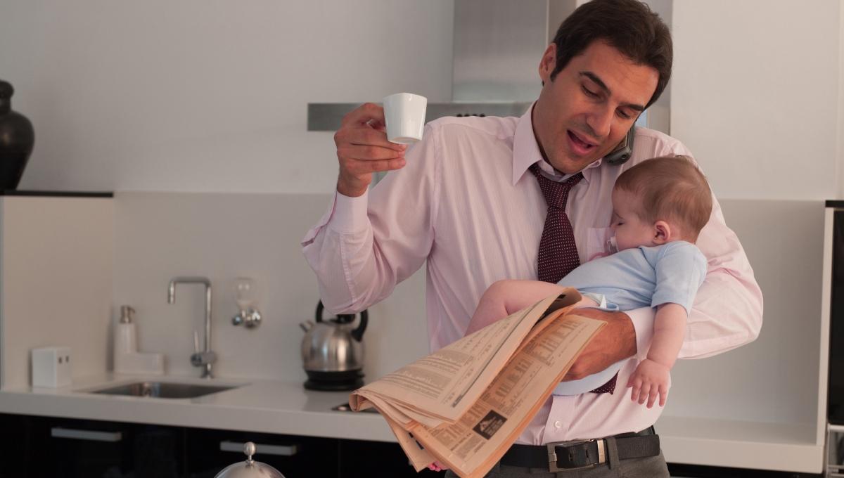 Father holding baby daughter while talking on phone in kitchen