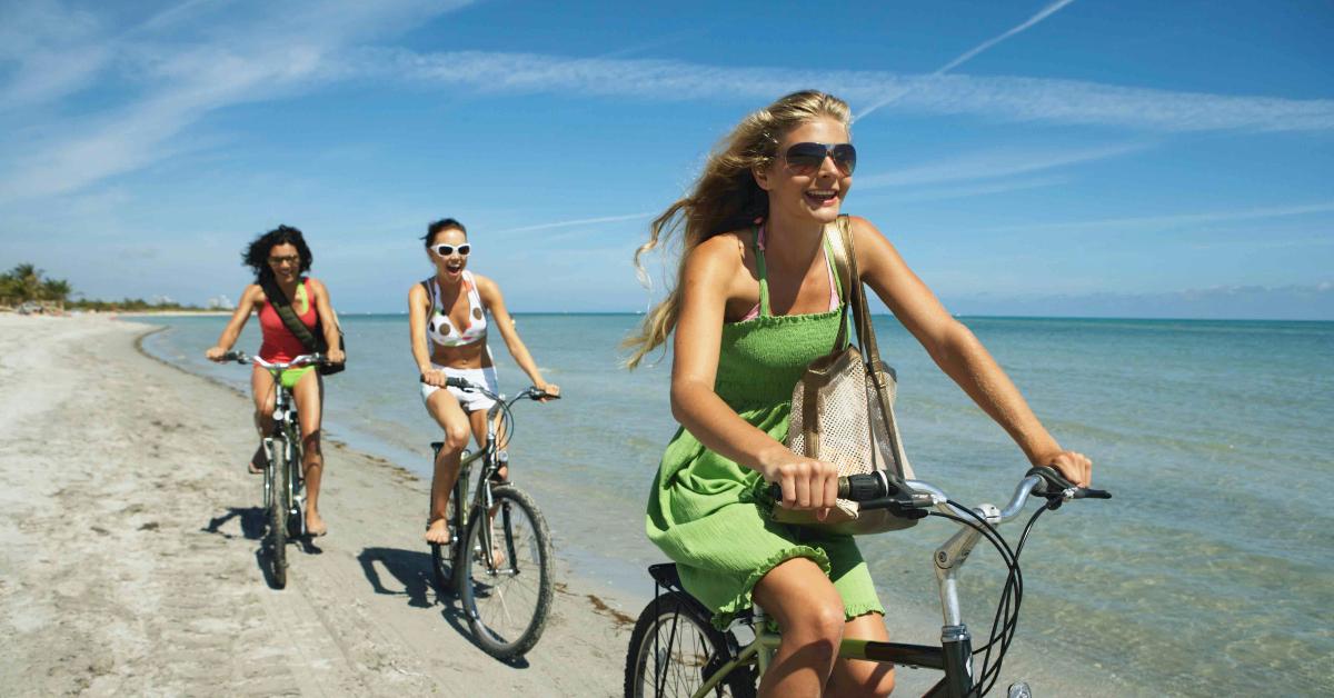 Three girls riding their bikes on the beach.