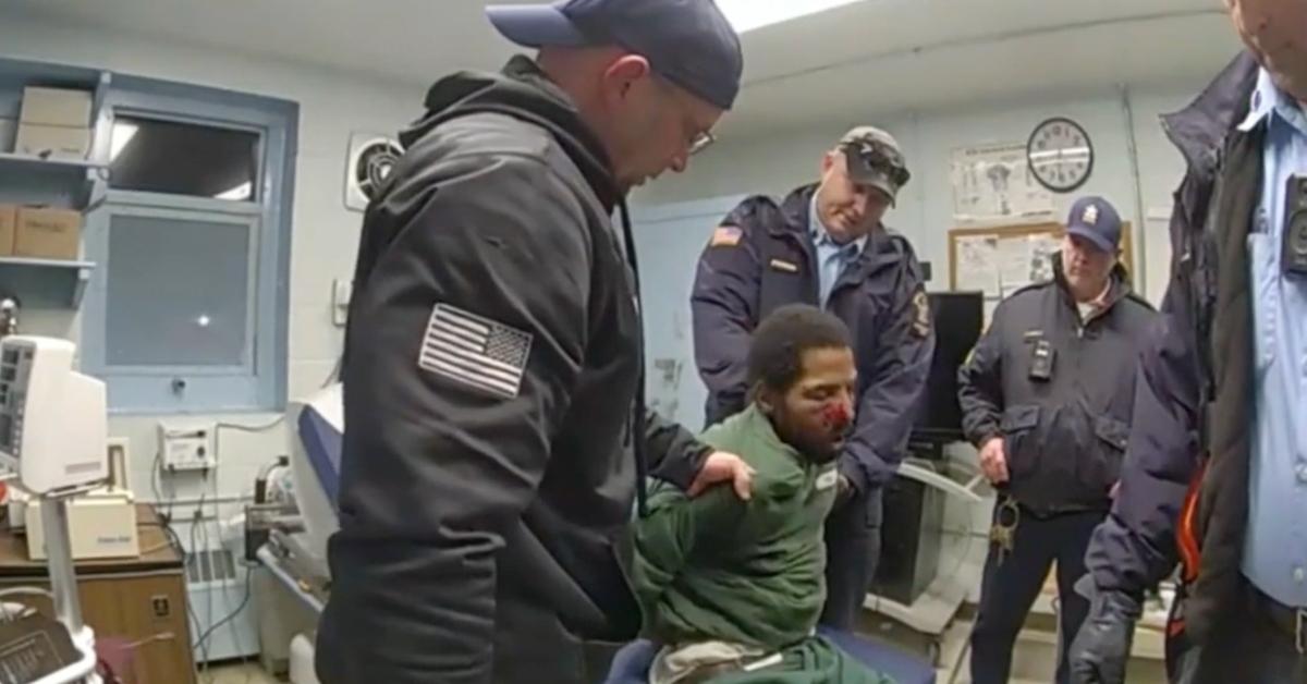 Robert Brooks (seated) in handcuffs with blood on his face, surrounded by four correctional officers