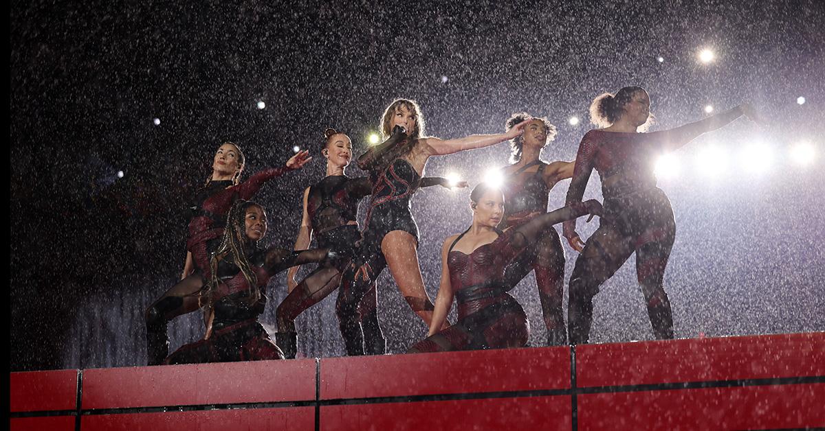 Taylor Swift on stage with backup dancers in the rain on the Eras Tour. 