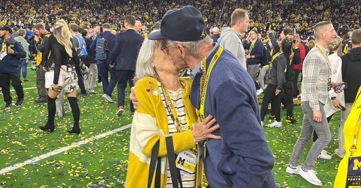 Jackie and Jack Harbaugh kiss on a football field.