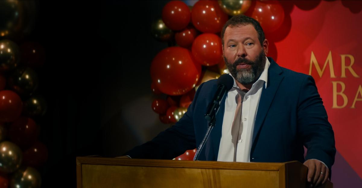 Bert speaks at a podium in front of a balloon backdrop in Free Bert.
