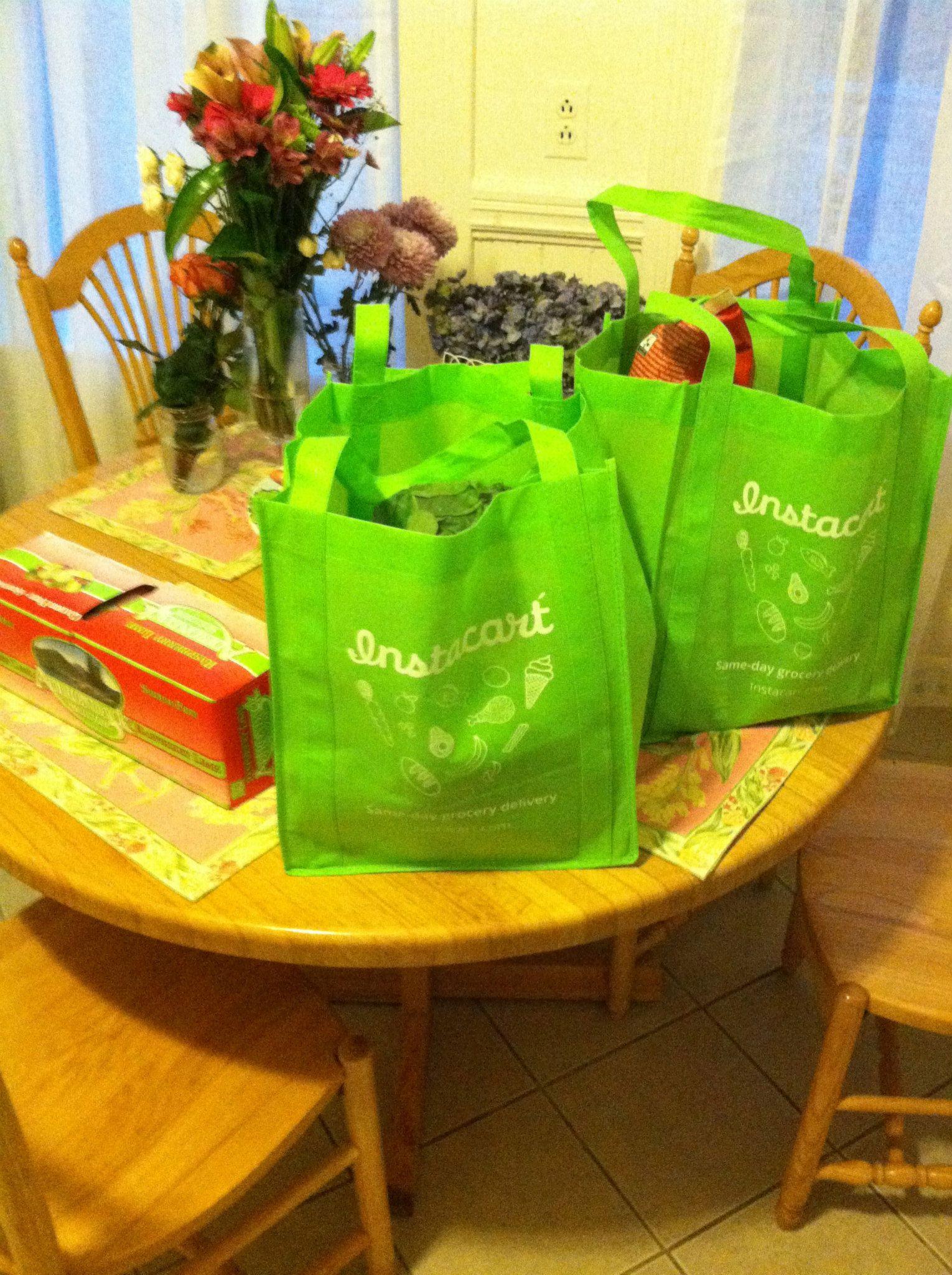 Green Instacart shopping bags with groceries inside on top of a kitchen table in a customer's home