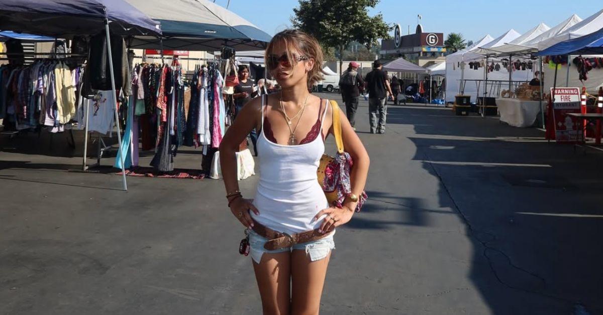 Emman Atienza in a white tank top and jean shorts in front of a flea market.