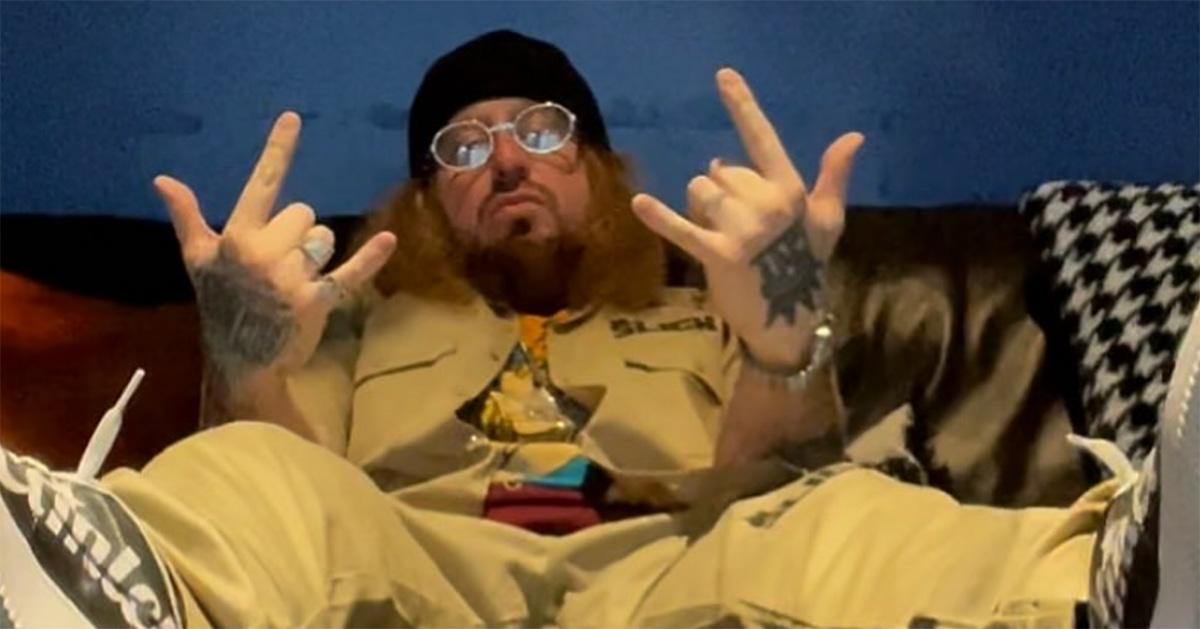 Rittz sitting with his hands in a rock on signal. 