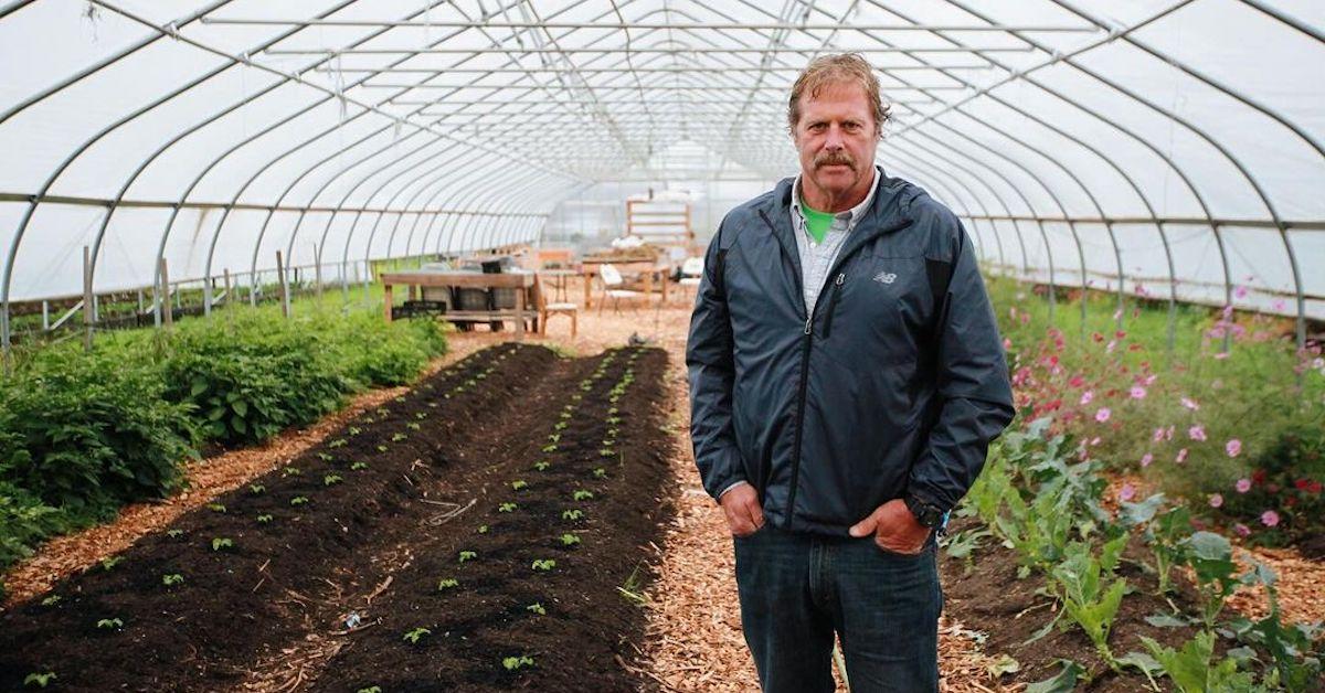 Roger Cook standing in a greenhouse wearing a windbreaker and jeans