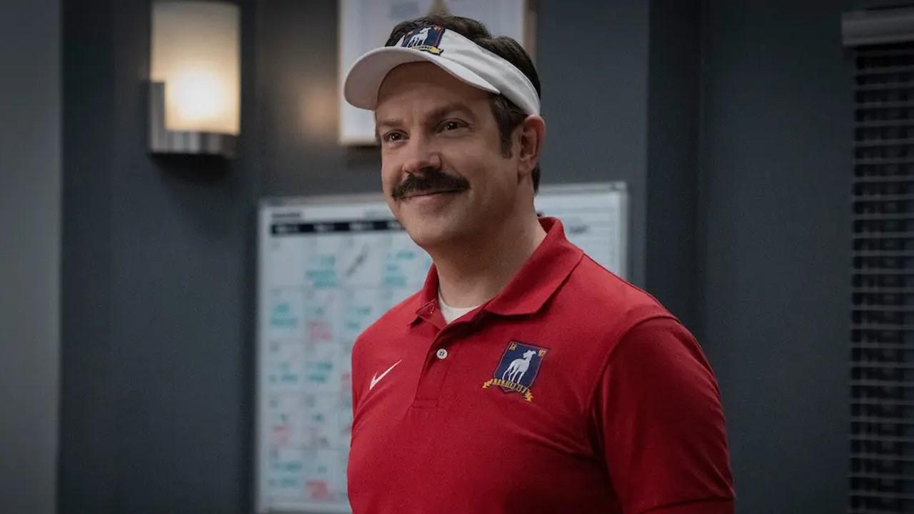 Ted Lasso smiling with a whiteboard behind him