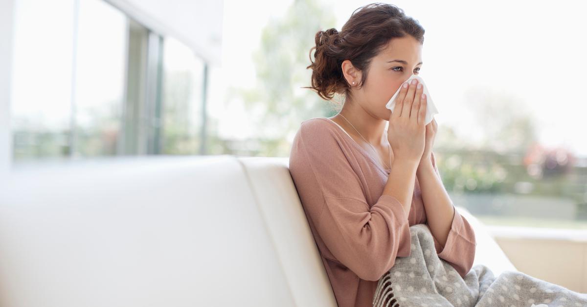 A sick woman blowing her nose and sitting on a couch