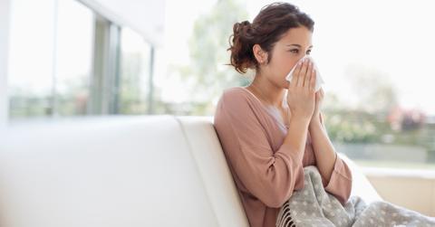A sick woman blowing her nose and sitting on a couch
