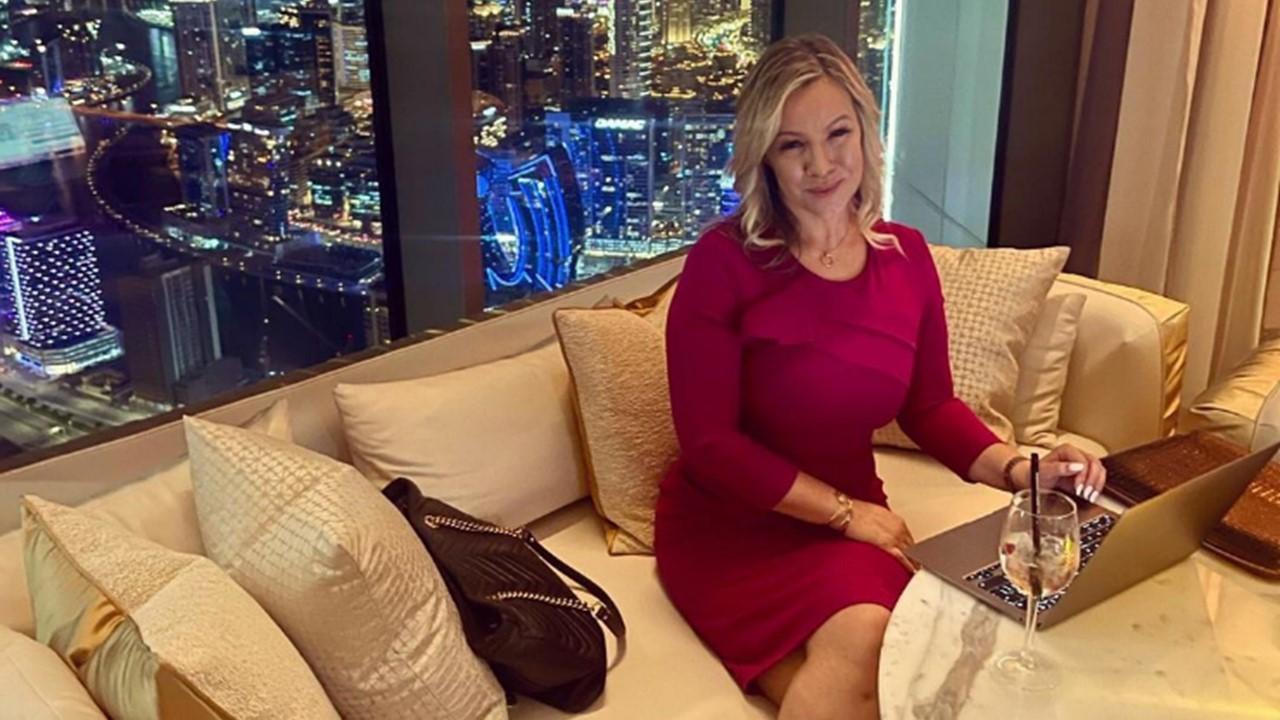 Maria Morris wearing a red dress and sitting on a gold couch