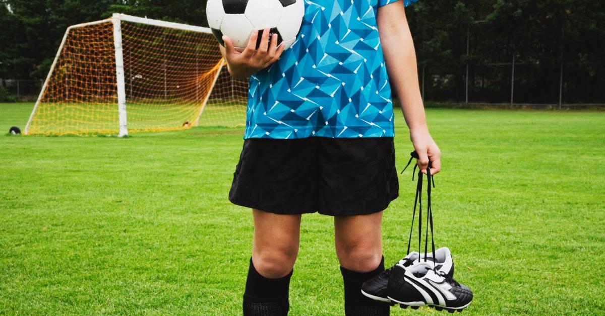 A  girl holding her soccer shoes on a soccer field.