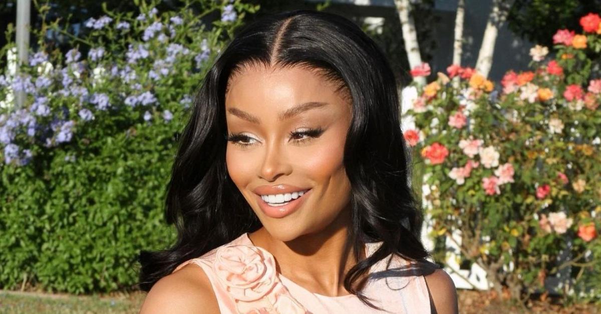 Blac Chyna wears peach-colored sleeveless shirt and smiles in front of a bed of flowers.