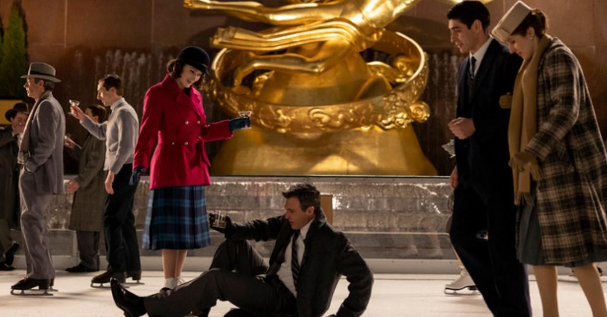 Miriam Maisel (Rachel Brosnahan) in a red coat, looks down on Gordon Ford (Reid Scott)  in a business suit on the ice