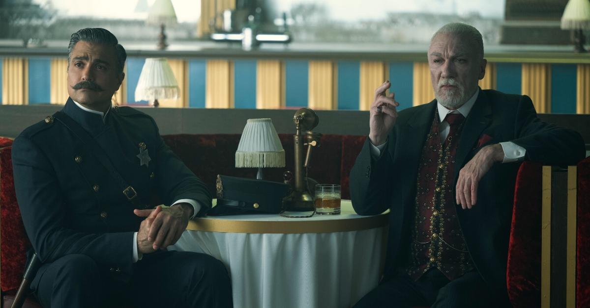 Jaime Camil as Sergeant Rivera and Patrick Page as Octavius Kratt sitting at the Kratt club looking devious on 'Schmigadoon'. 