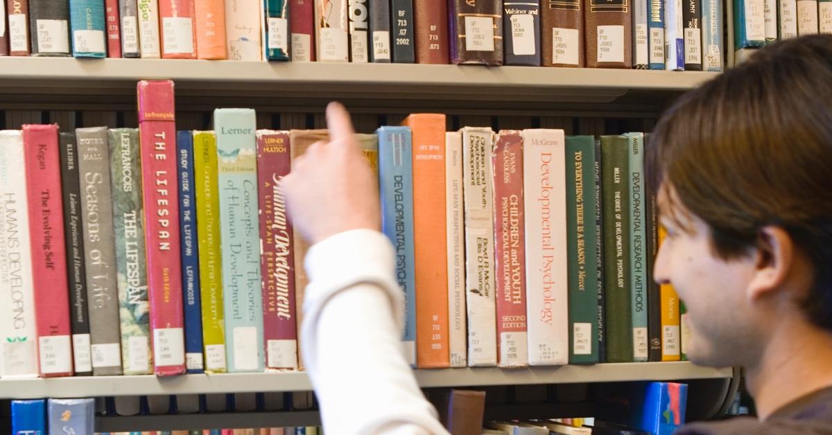 Man checking out a library book from a shelf.