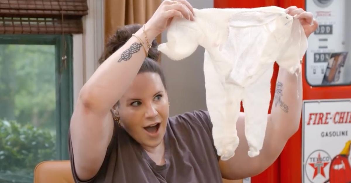 Whitney Thore holding up baby clothes.