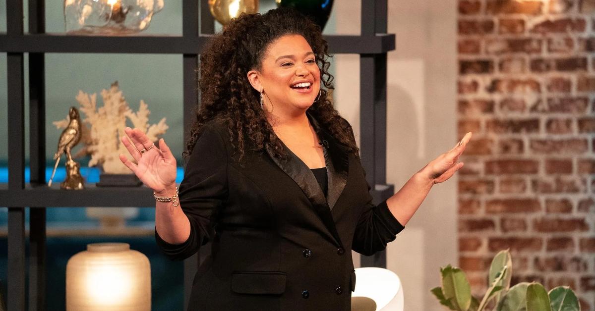 Michelle Buteau meets the cast in front of a shelf and brick wall on The Circle