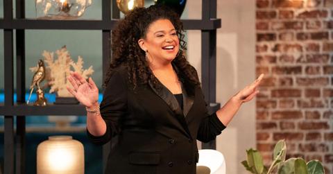 Michelle Buteau meets the cast in front of a shelf and brick wall on The Circle