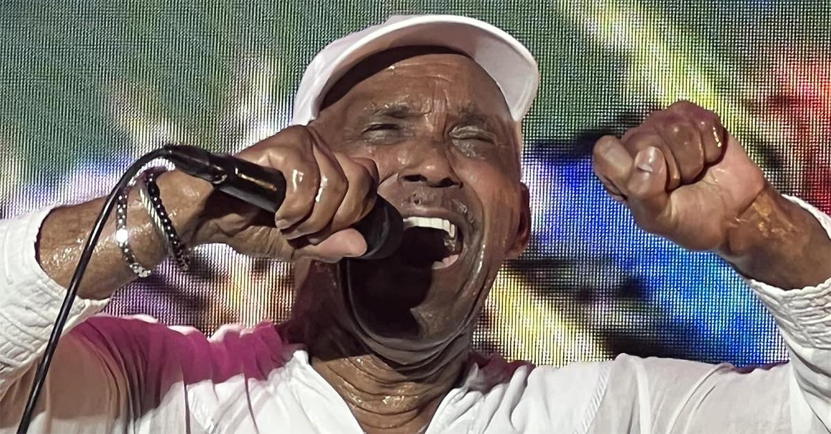 Frankie Beverly singing into a microphone in a white shirt. 