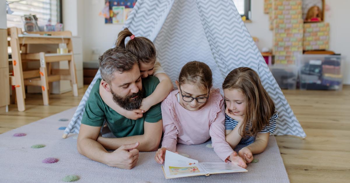 A dad and his three daughters reading a book together.