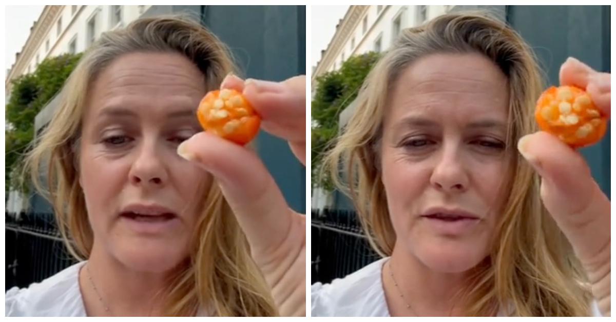 Alicia Silverstone holds up a tomato-like fruit to her phone camera on TikTok. 