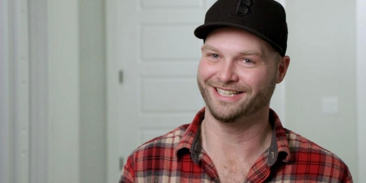 John from 90 Day Fiancé smiles in a hallway