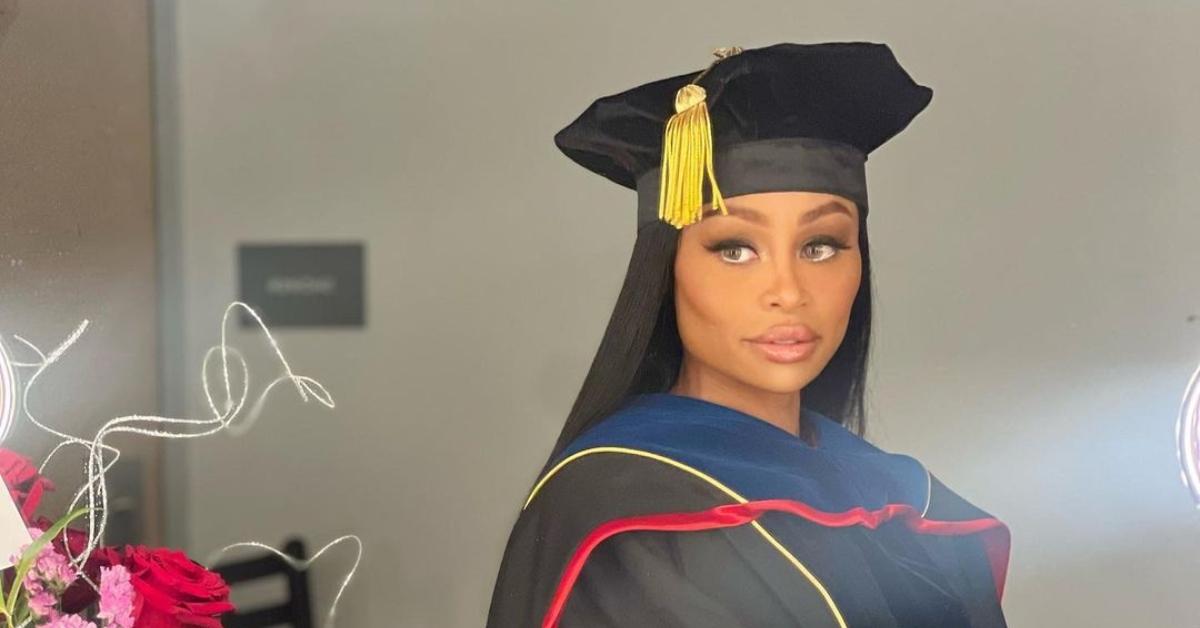 Blac Chyna wears Graduation hat and robe next to a a bouquet of flowers.