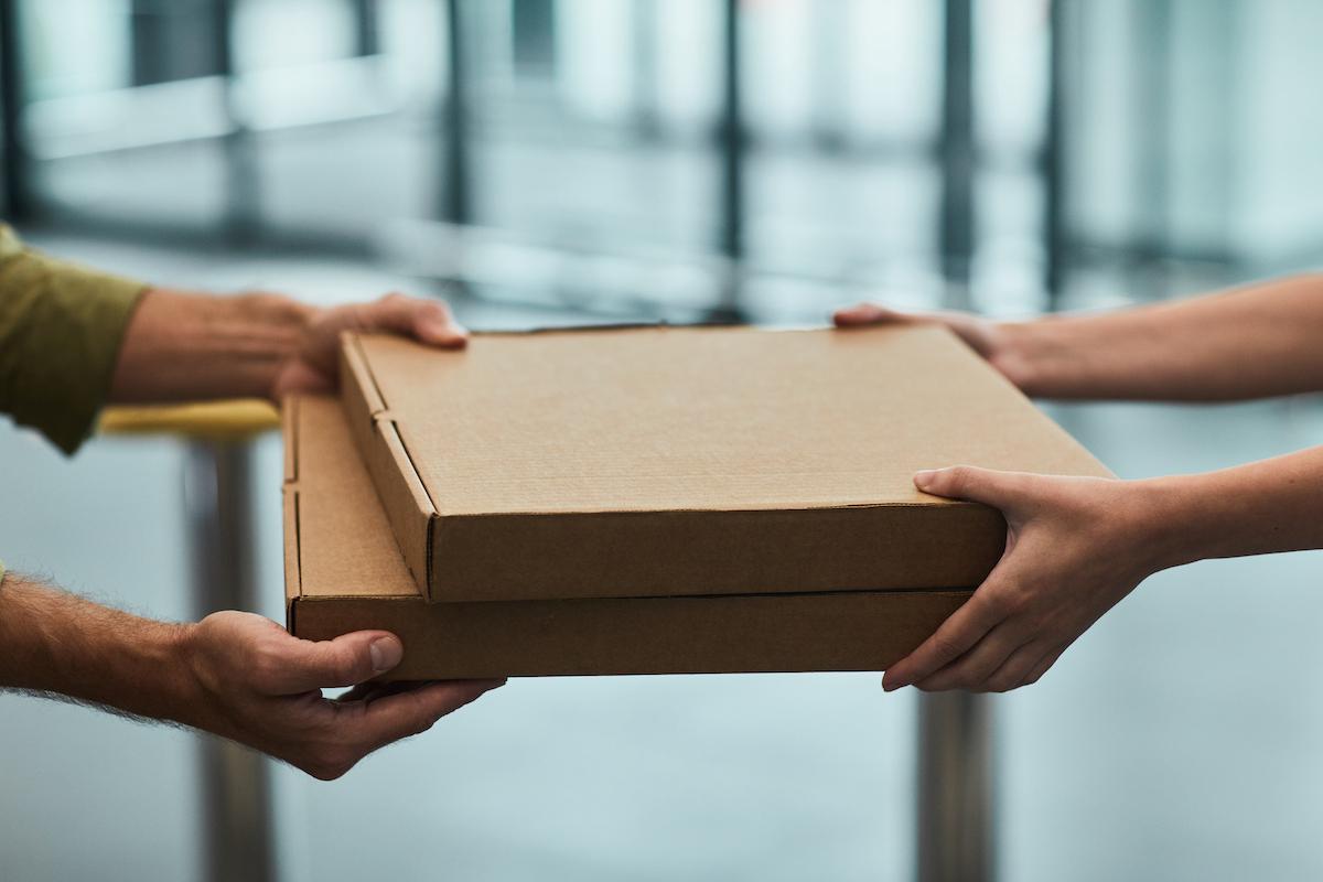 One person handing two pizza boxes to another person.