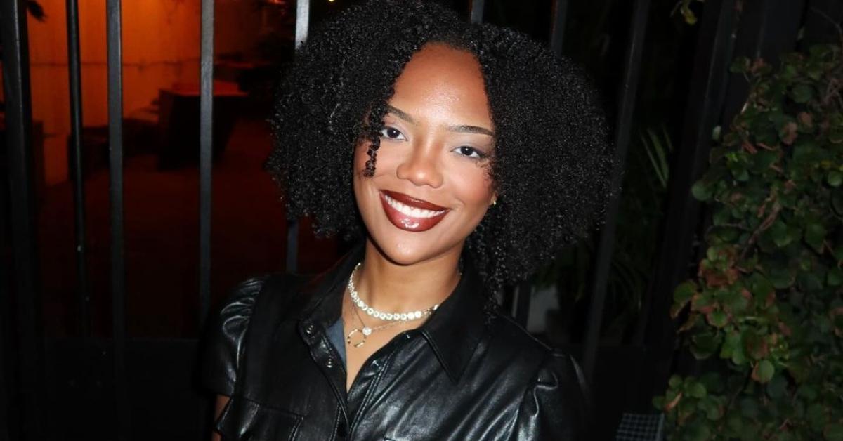 Riley Burruss in a black leather dress in front of a gate and potted plant