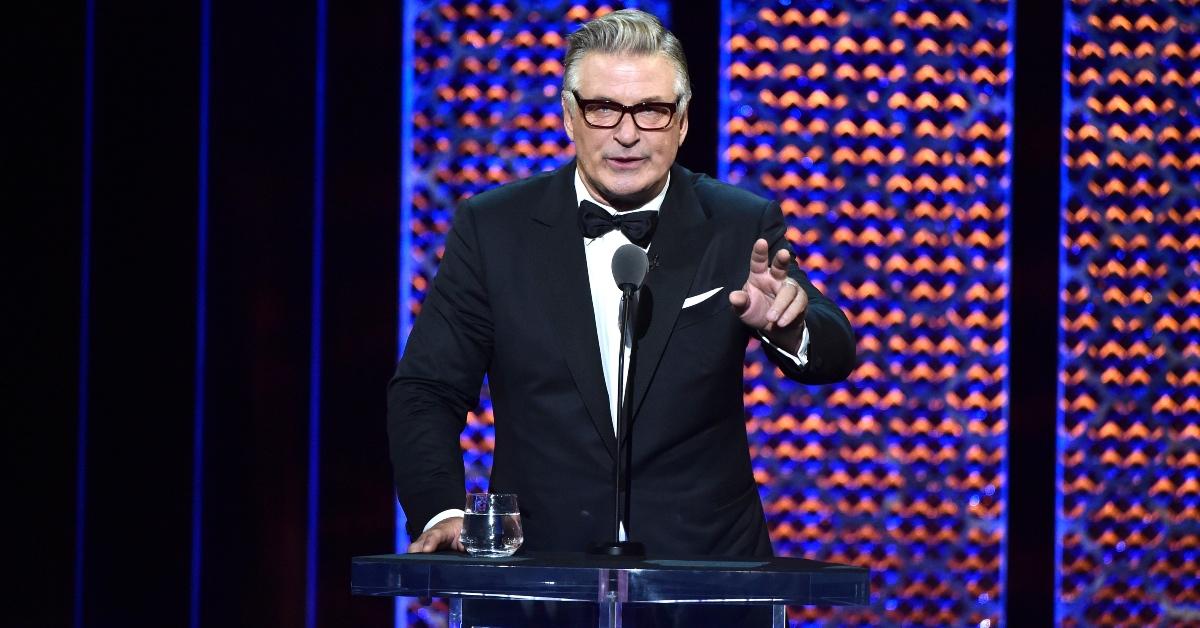 Actor Alec Baldwin speaks at an awards show wearing glasses. 