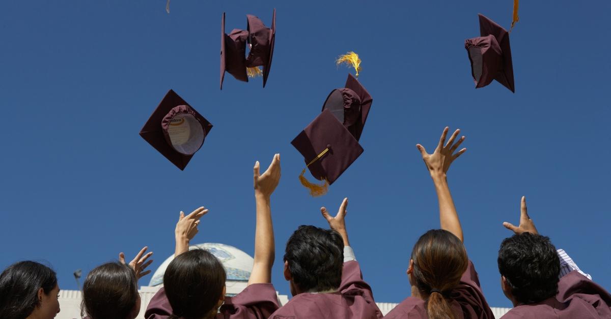 Graduate students throwing mortar boards, outdoors, rear view - stock photo