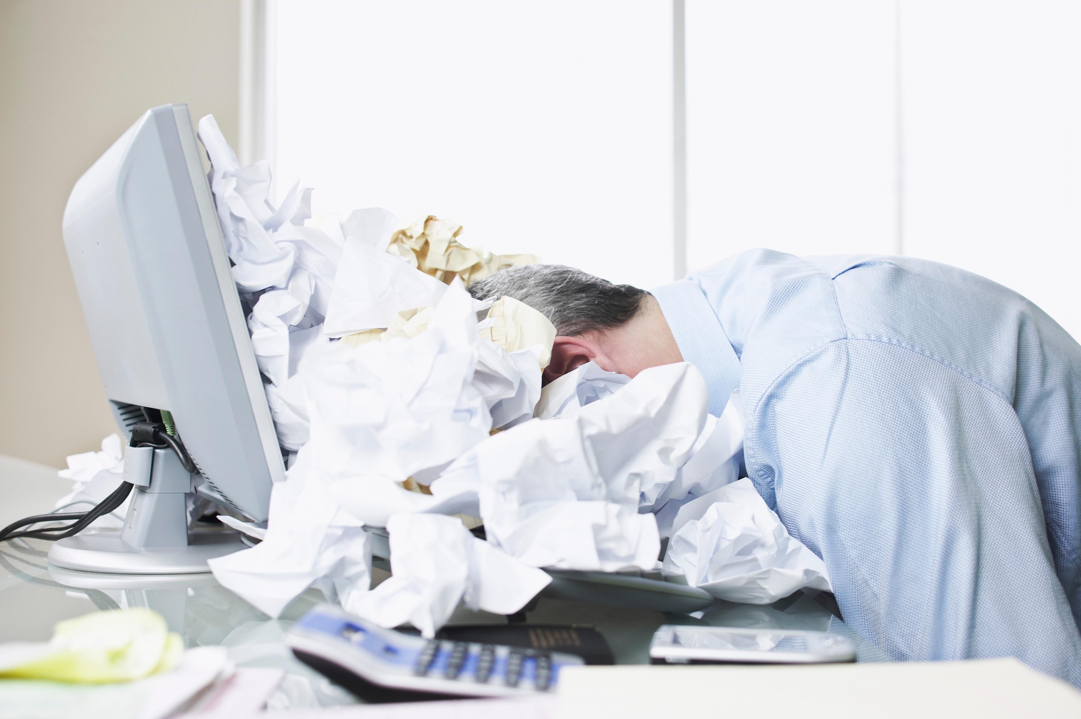 Businessman face down in a pile of crumbled up papers