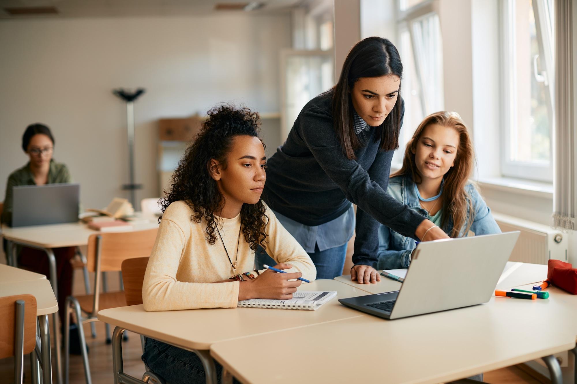 A high school teacherr assisting her students in e-learning on laptop in the classroom