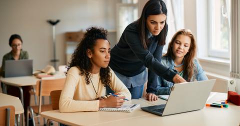 A high school teacherr assisting her students in e-learning on laptop in the classroom