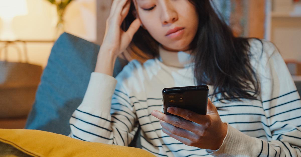 A woman looking at her phone with her hand on her head. 